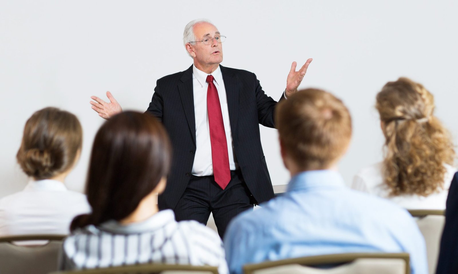 Portrait of senior manager standing in front of audience in conference room, making presentation to his young colleagues